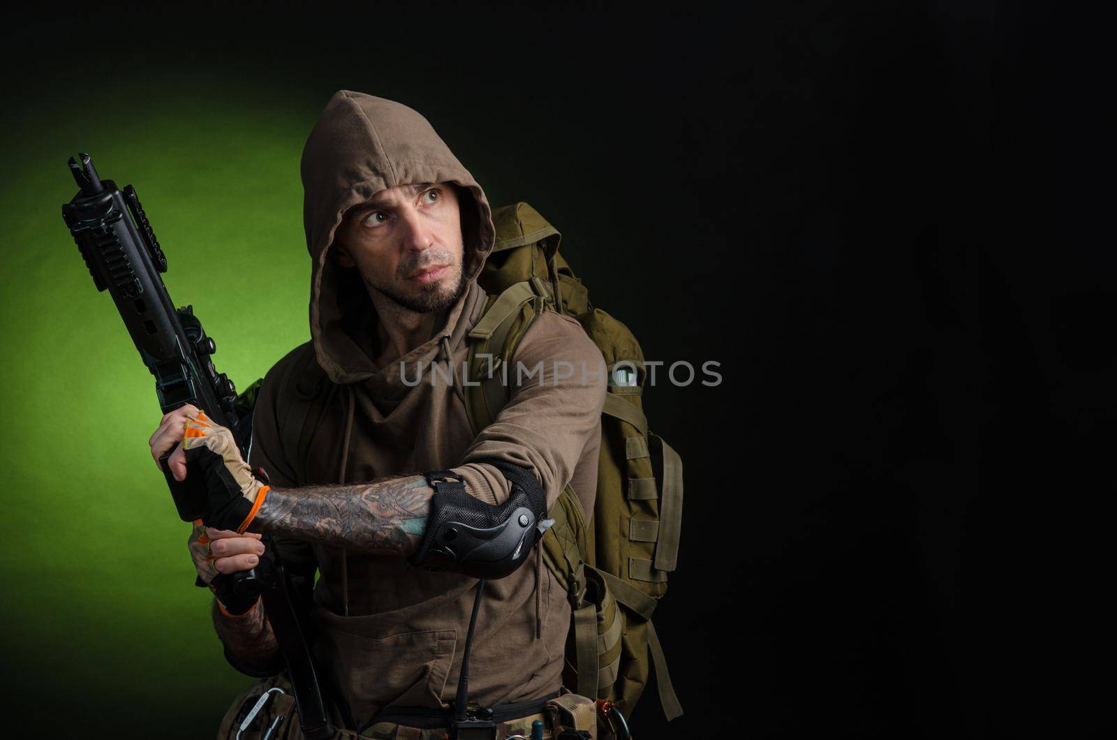 man Stalker with a gun with an optical sight and a backpack on a dark background with emotions looking, aiming, watching, sneaking