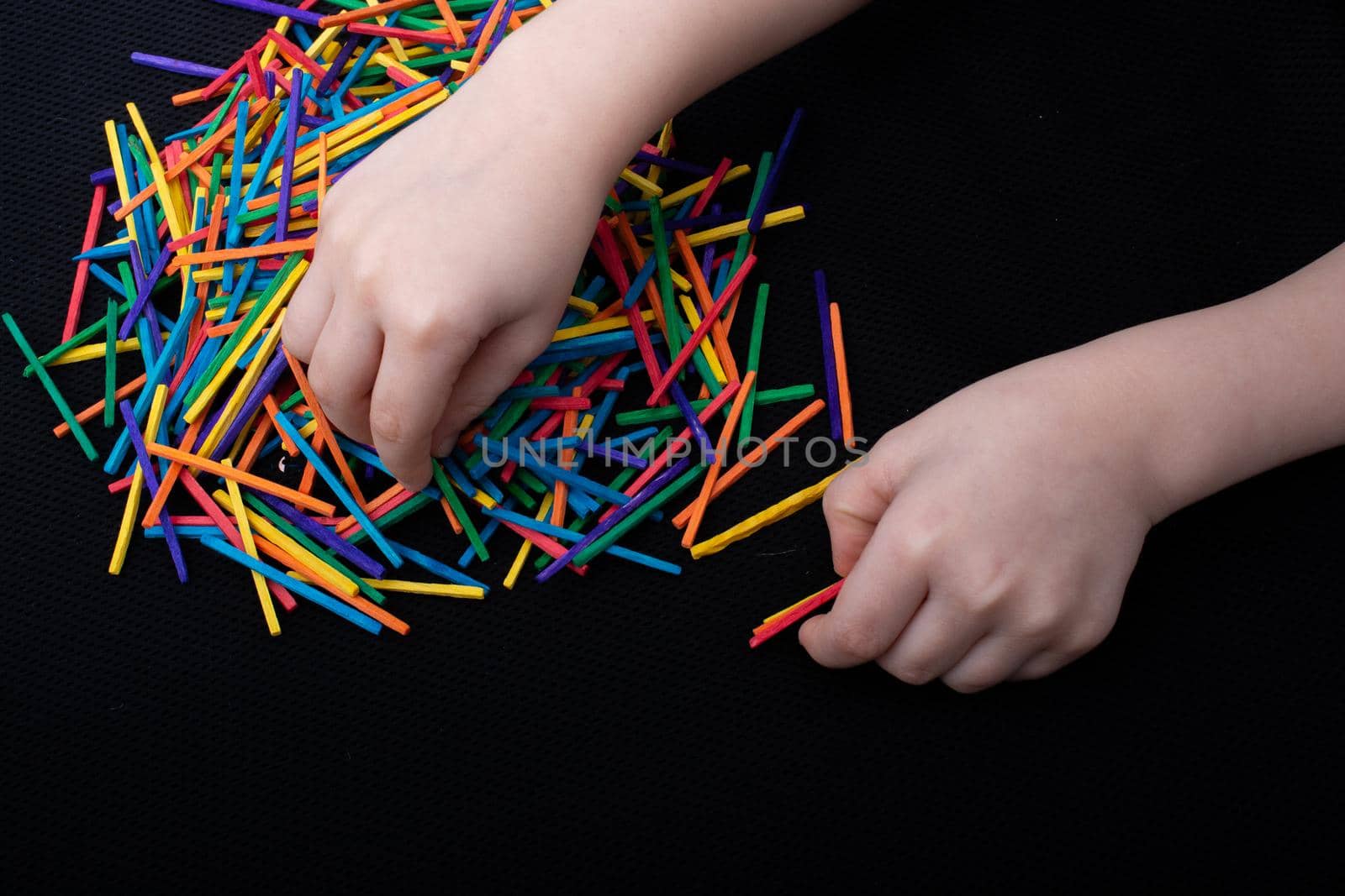 Kid playing with coloured wooden  sticks for creativity on white background