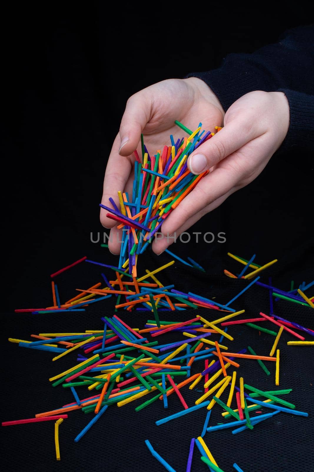 Hand letting coloured wooden  sticks drop on black by berkay