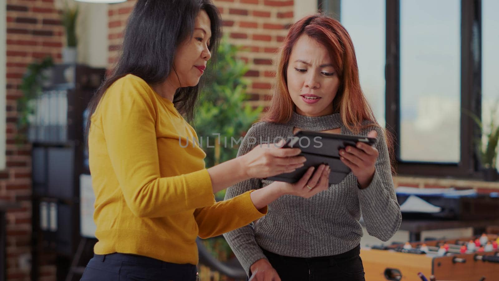 Business partners using tablet and research files in startup office to work on management project. Team of women working together to develop financial strategy and plan success.