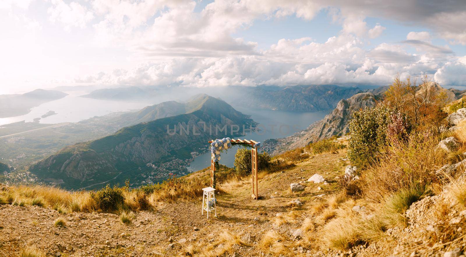 Simple wooden arch decorated with flowers stands on top of a mountain overlooking the valley. High quality photo