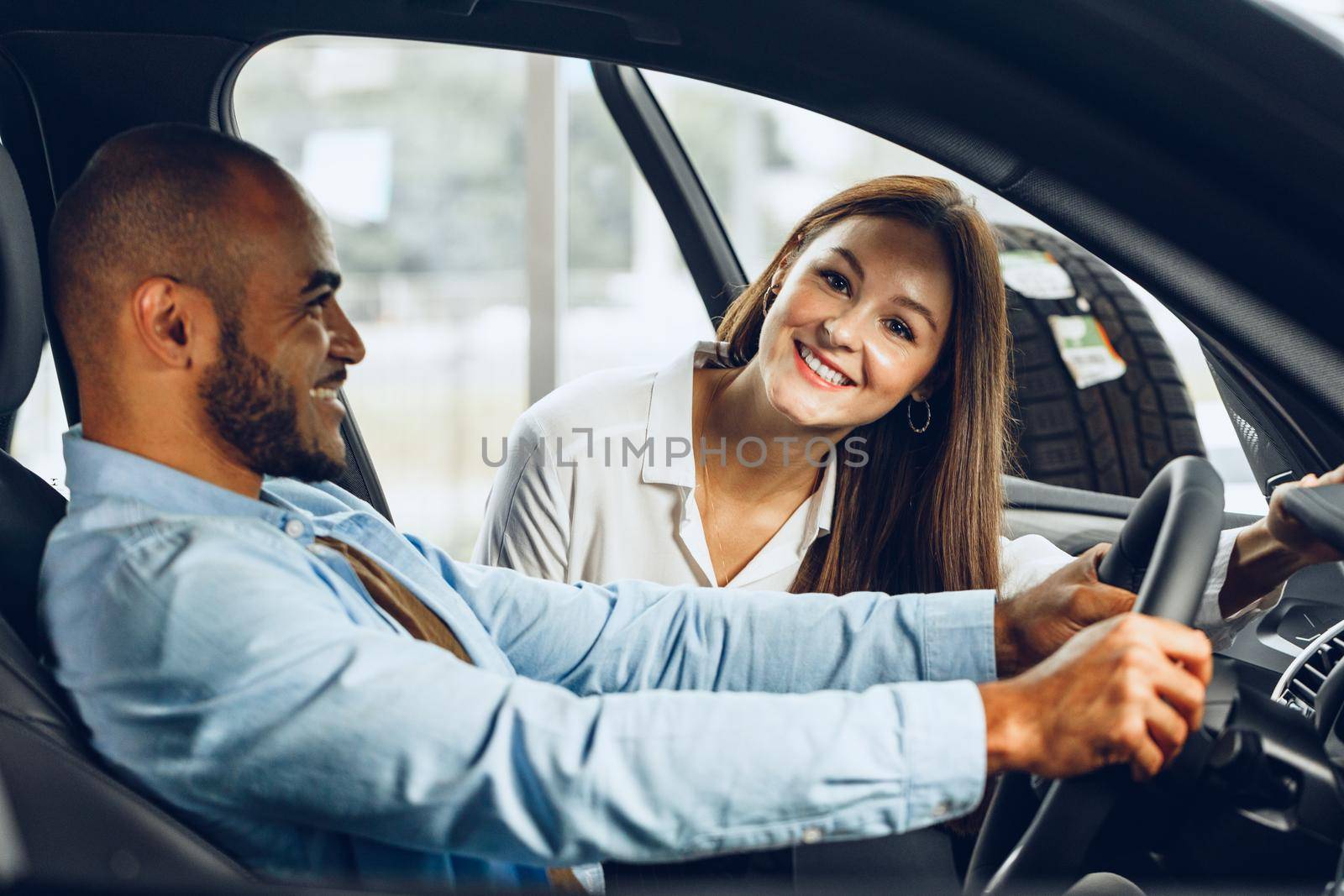 Young woman salesperson in car showroom showing a car to her male client close up