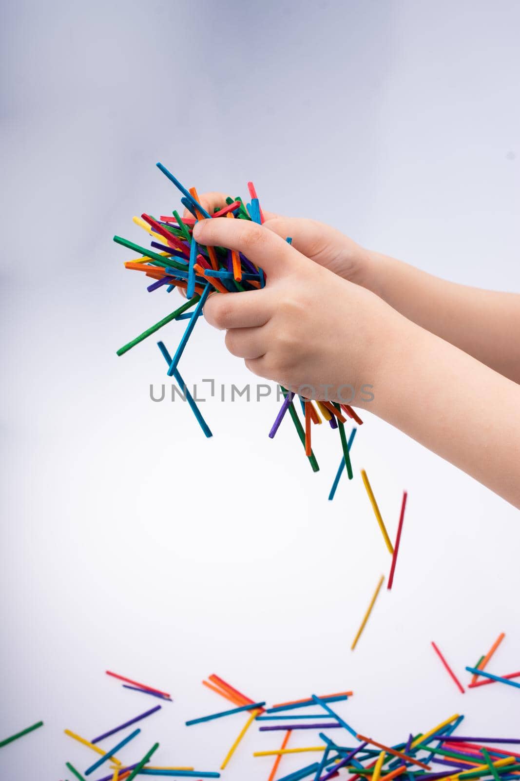 Hand letting coloured wooden  sticks fall on white background
