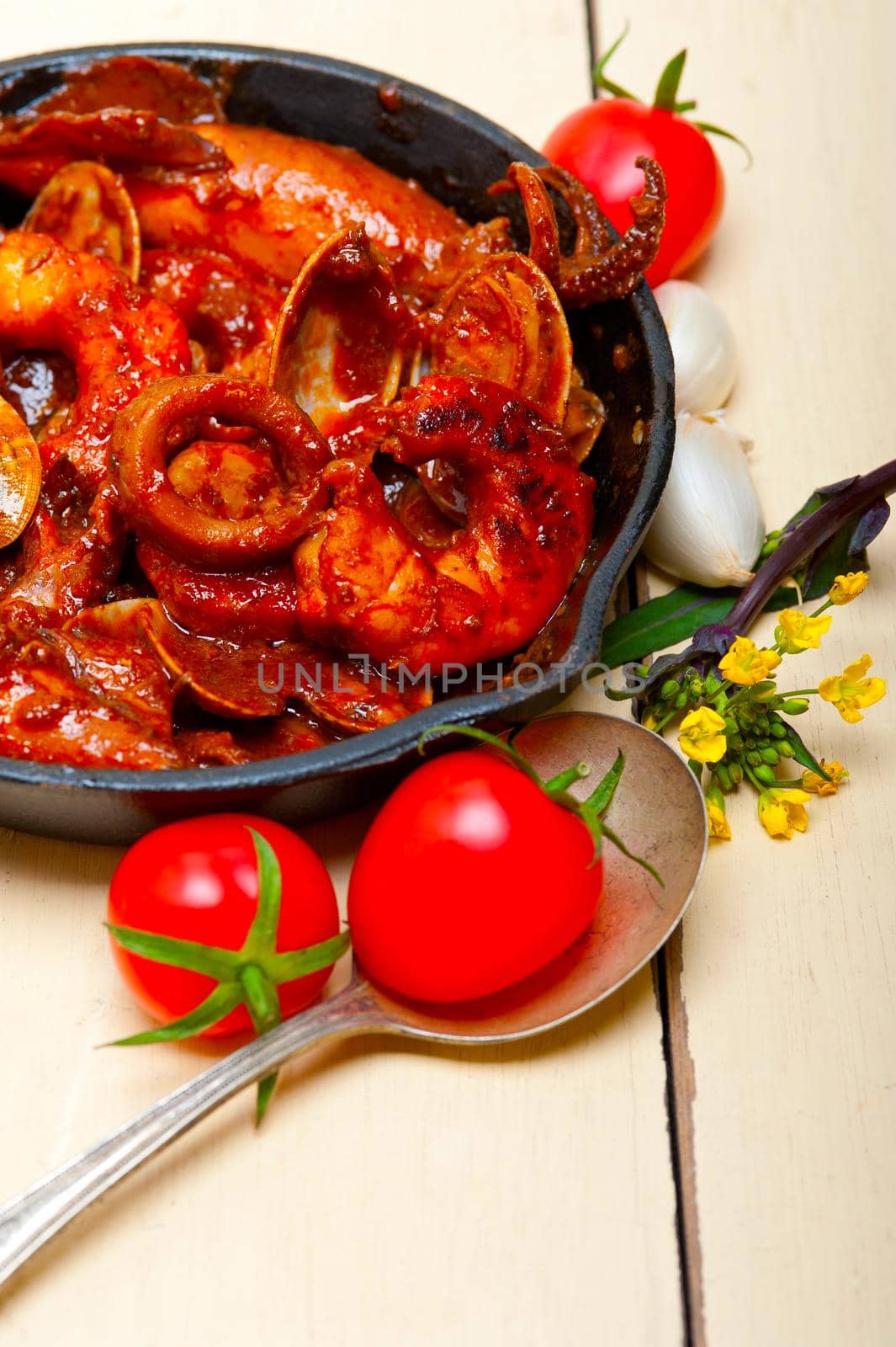 fresh seafood stew prepared on an iron skillet ove white rustic wood table 