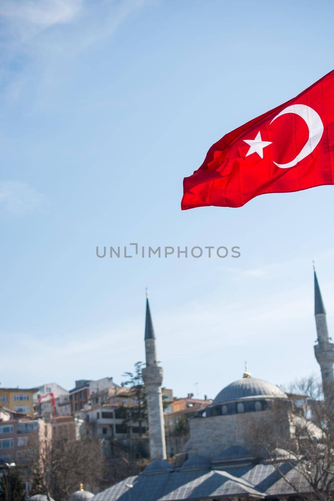 Turkish national flag hang on a pole on a rope with a minaret behind