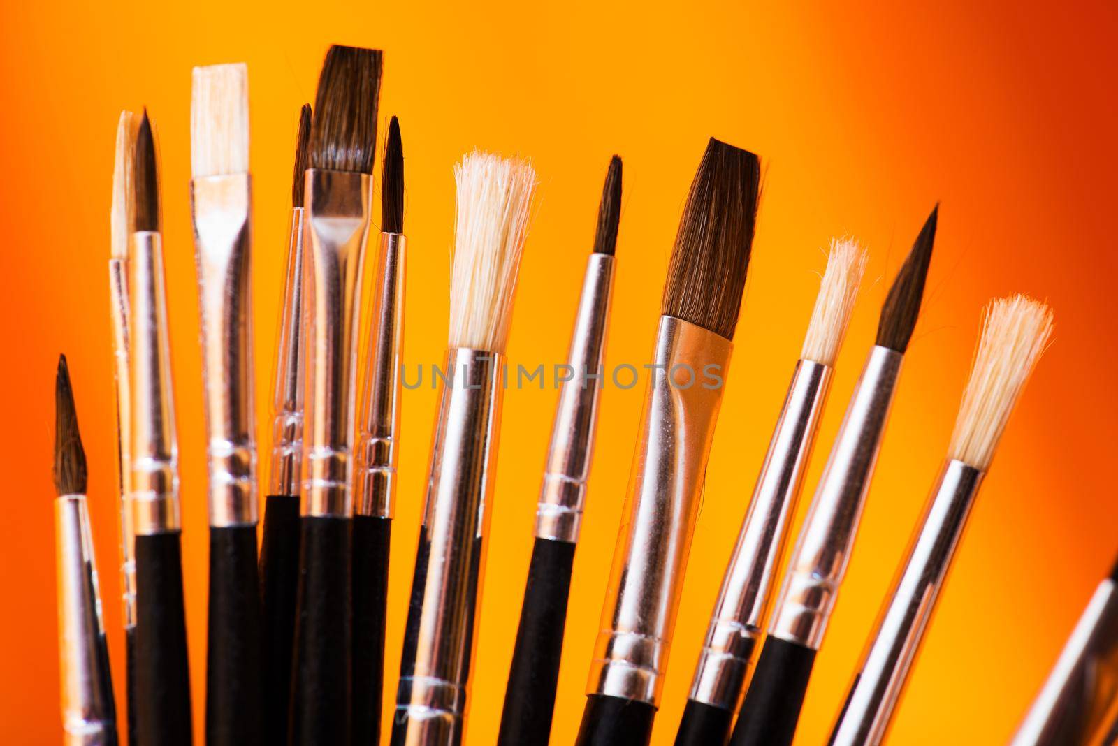 The Right Paintbrush. Many Types of Synthetic Paintbrushes on Orange-Red Background. Paintbrushes Closeup Photo.