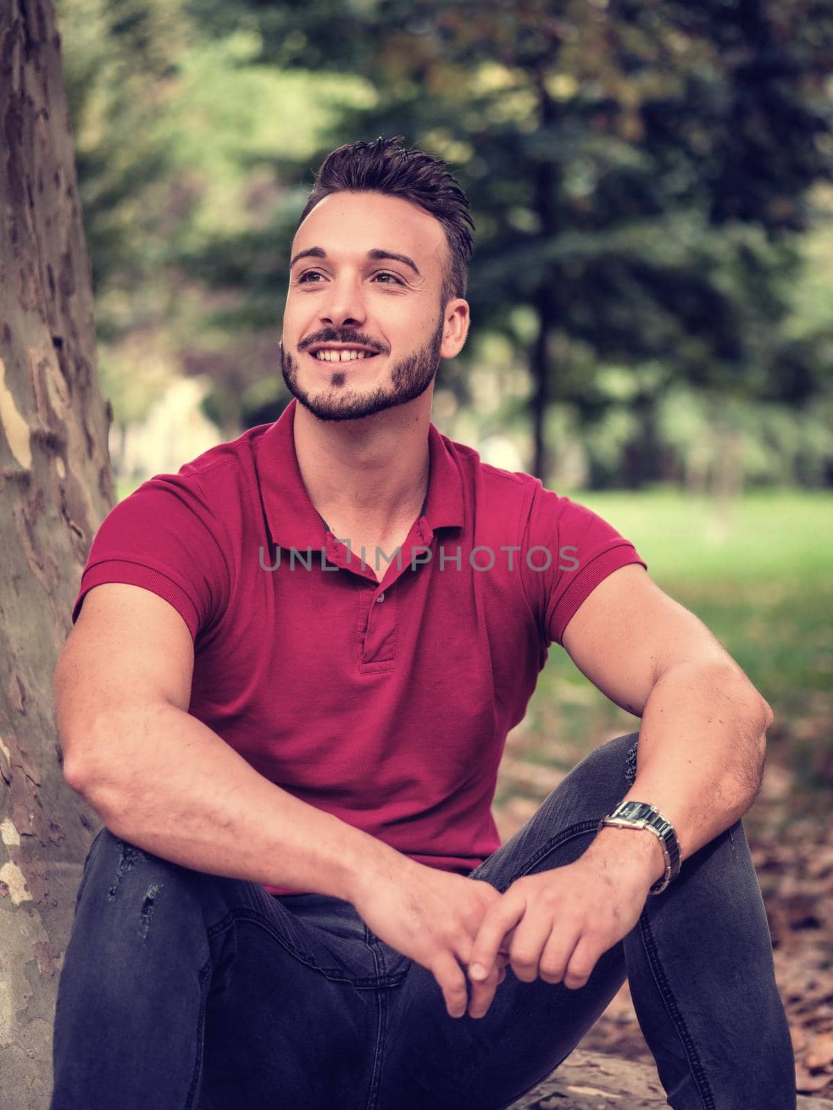 Attractive young man in park resting or relaxing against tree, in a sunny summer day