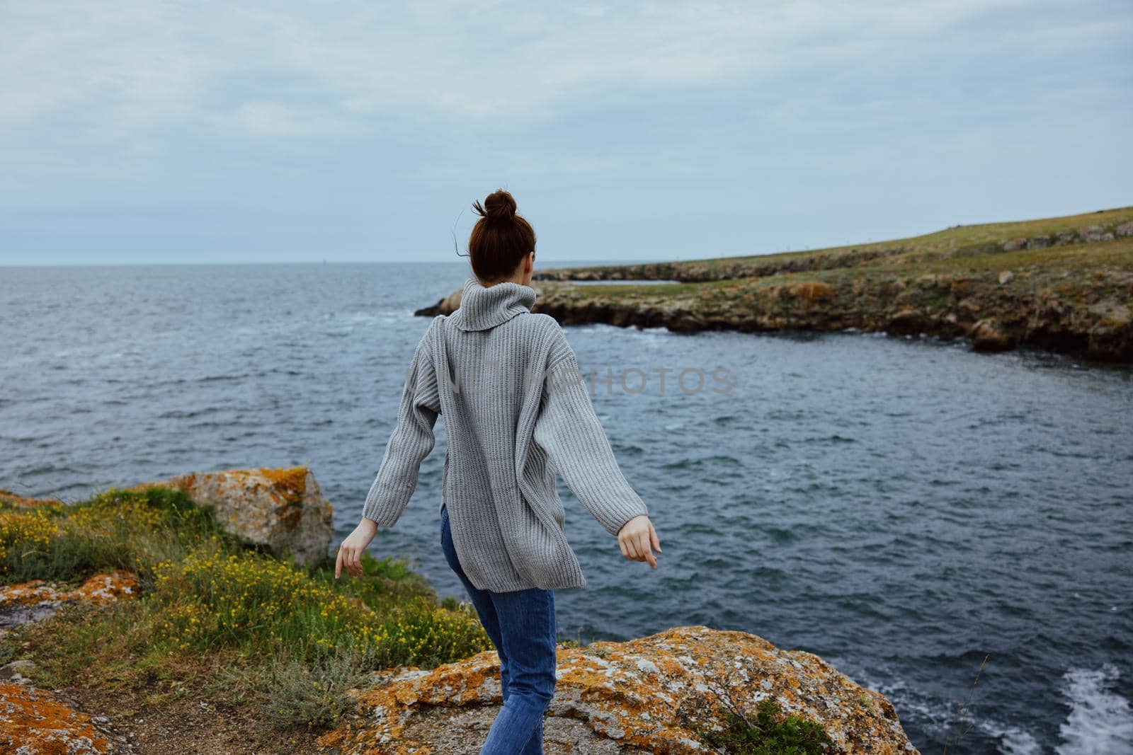 beautiful woman in a gray sweater stands on a rocky shore nature Relaxation concept. High quality photo