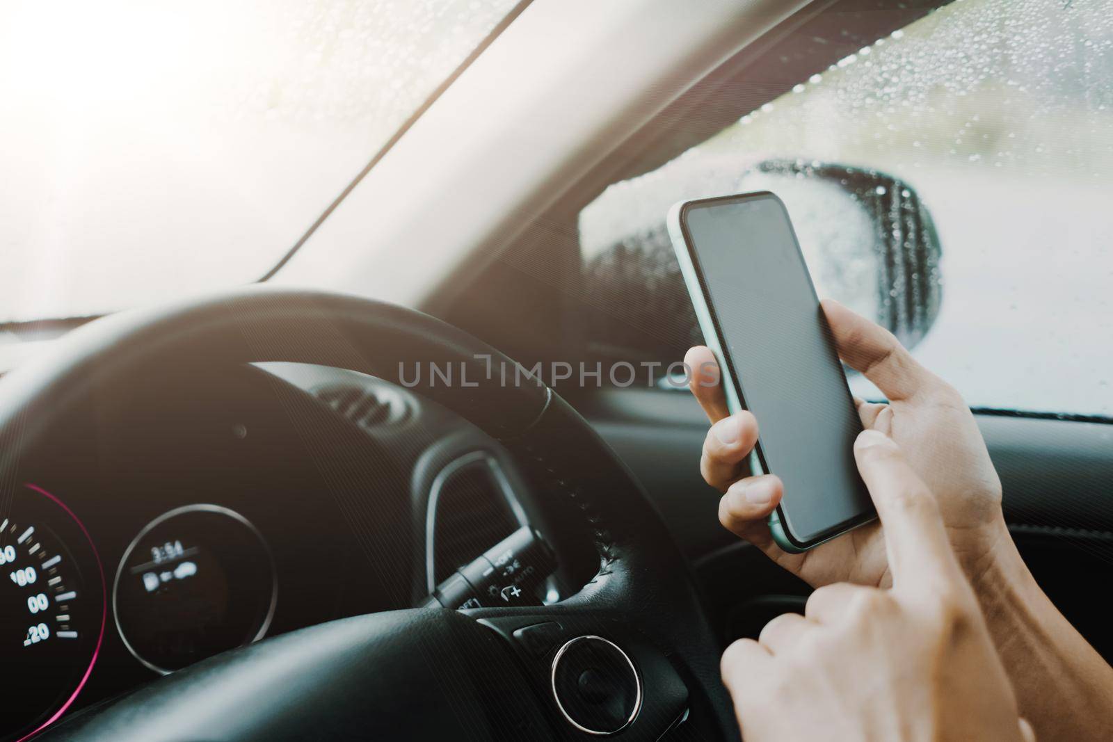 Hand of woman on steering wheel drive a car while using smartphone sunlight background.
