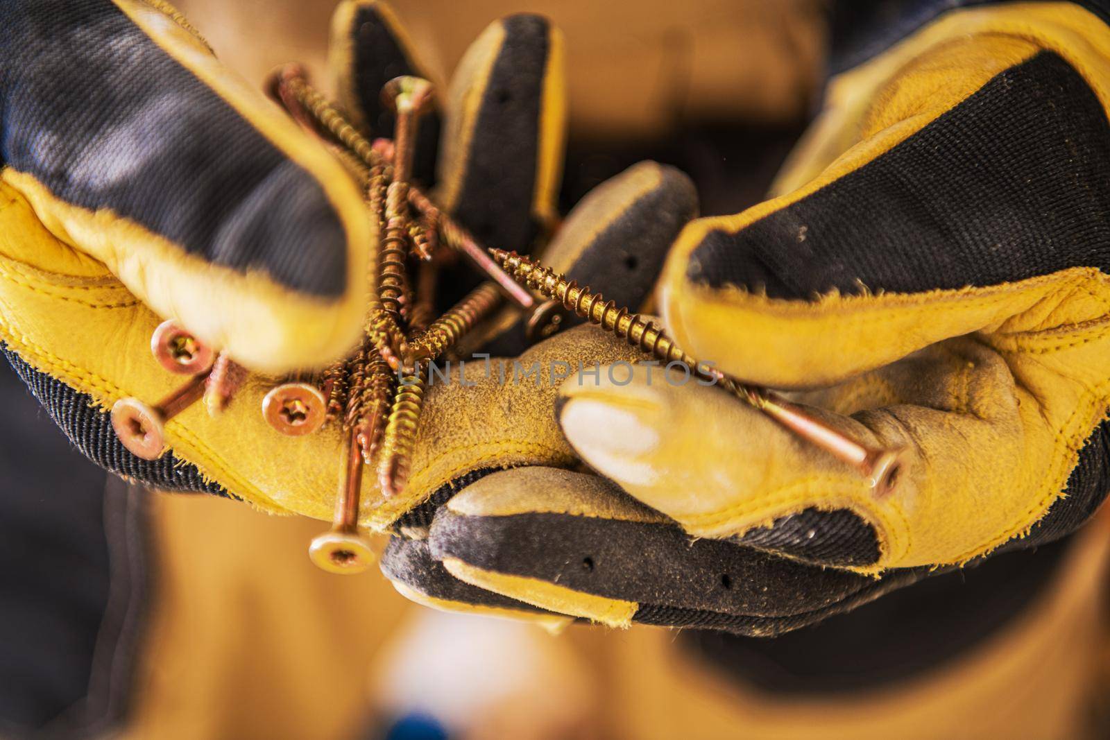 Close Up Of Construction Worker Hands In Gloves Holding Bunch Of Golden Long Screws. 