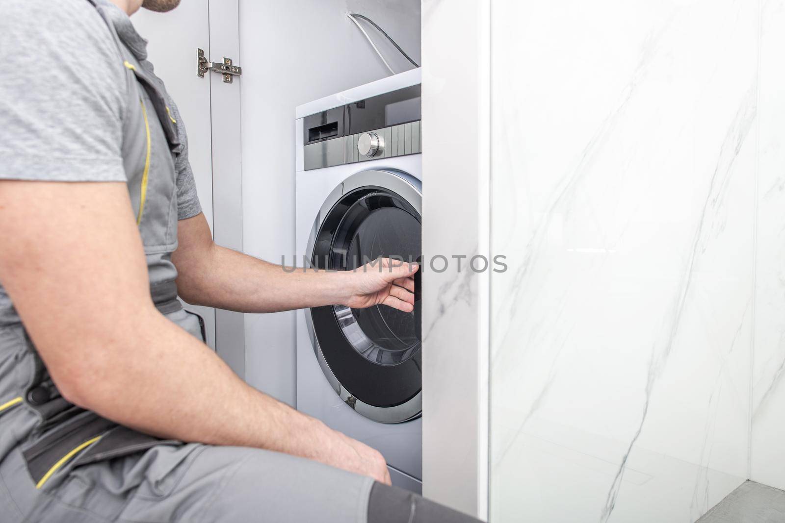 Washing Machine Installation by Caucasian Appliances Technician. Laundry Machine Inside Bathroom Cabinet. by welcomia
