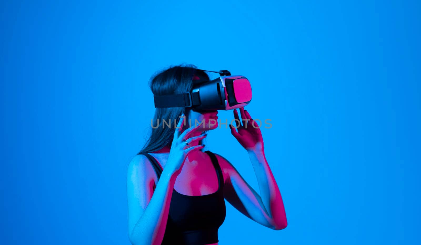 Portrait of young woman playing in VR-glasses in neon light on blue background. Concept modern gadgets and technologies. Future technology concept. Virtual reality gaming. by vovsht