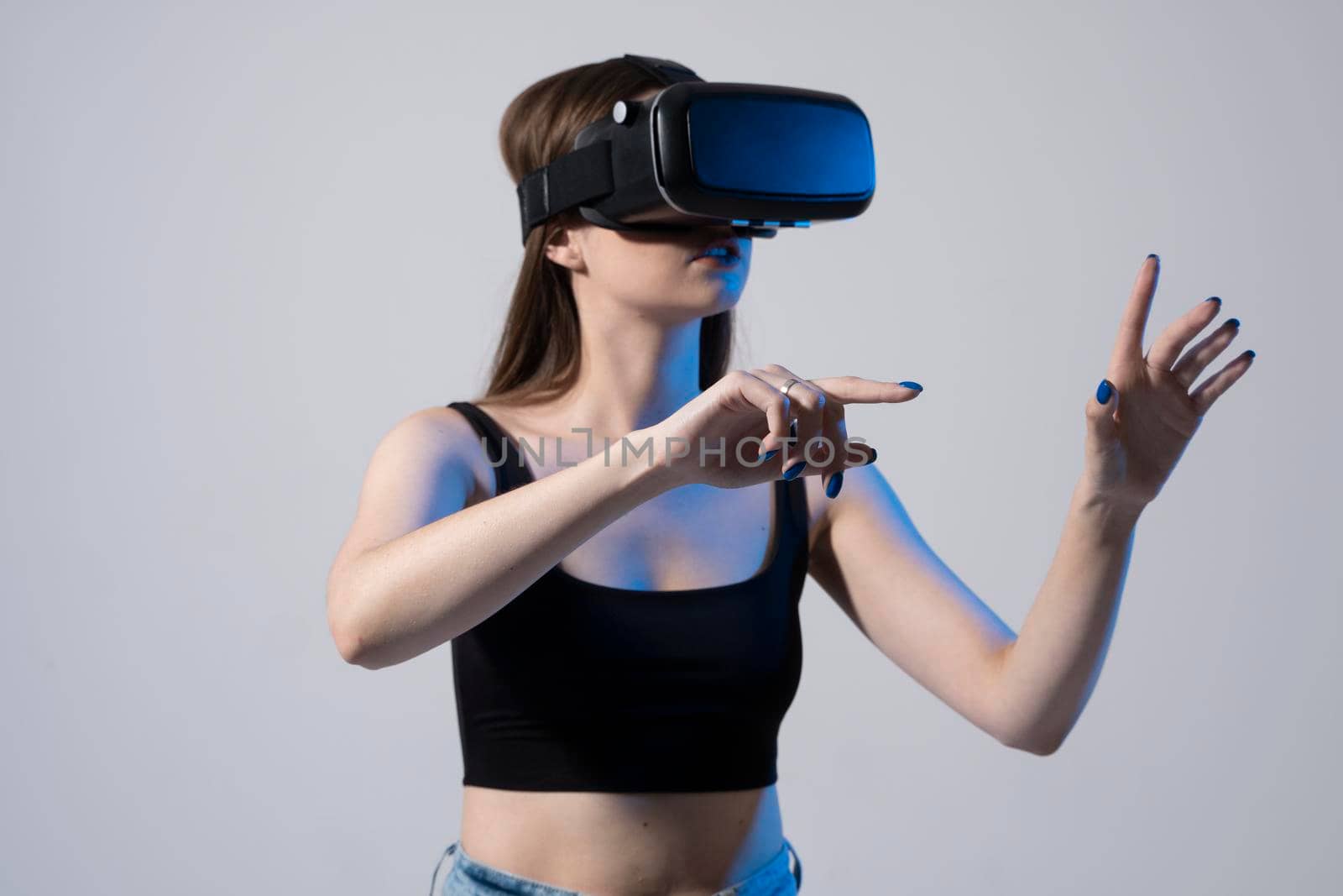 Close up of young woman stands in studio wearing VR glasses and swiping scrolling zooming with hands in a virtual space while interacting with a objects in a social networks