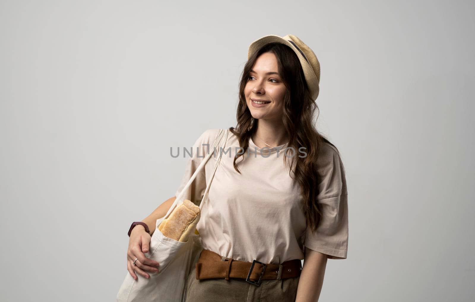 Smiling young woman in light summer clothes with a mesh eco bag full of vegetables, greens watching in a camera on a white studio background. Sustainable lifestyle. Eco friendly concept. Zero waste. by vovsht