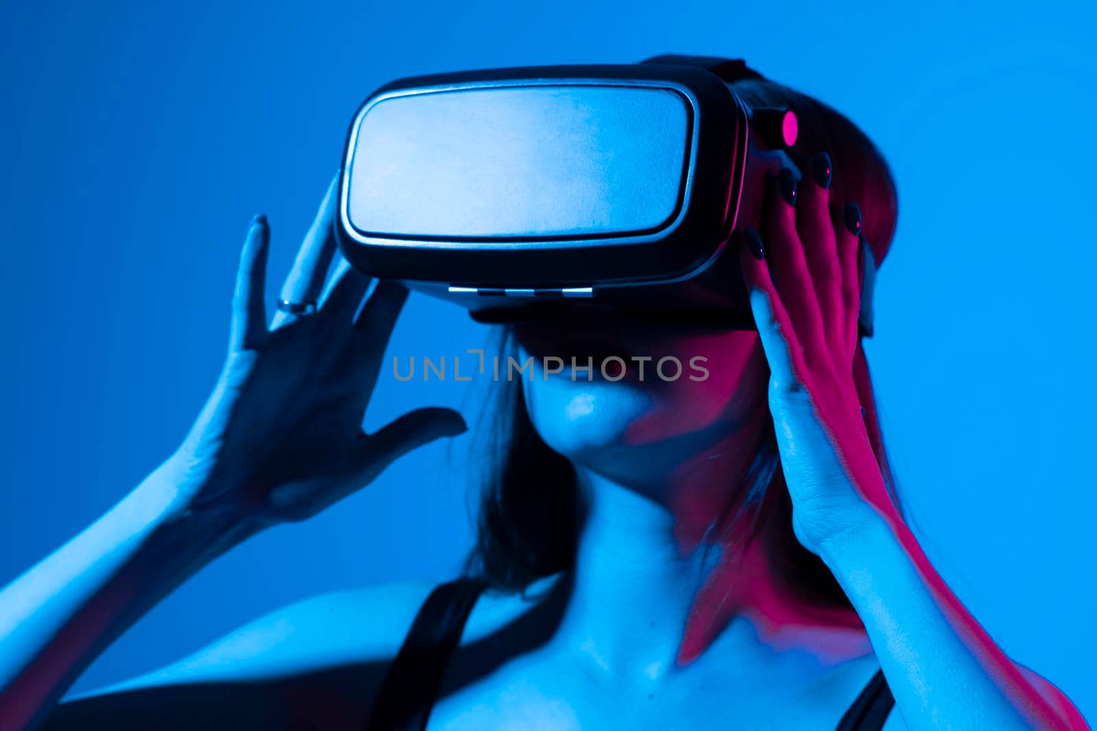 Young woman using VR headset helmet to interacts with metaverse using swipe and stretching gestures. Watching virtual reality 3d video. Girl in VR goggles looking around. by vovsht