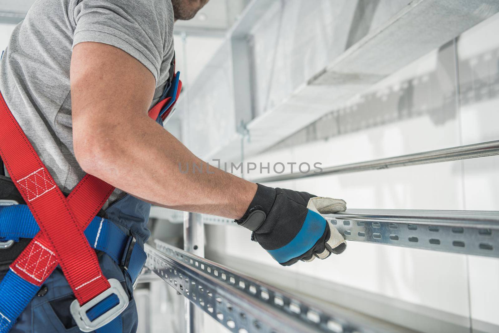 Caucasian Worker Moving Aluminium Frame Elements Inside Warehouse Close Up. Safety Harness Equipment.