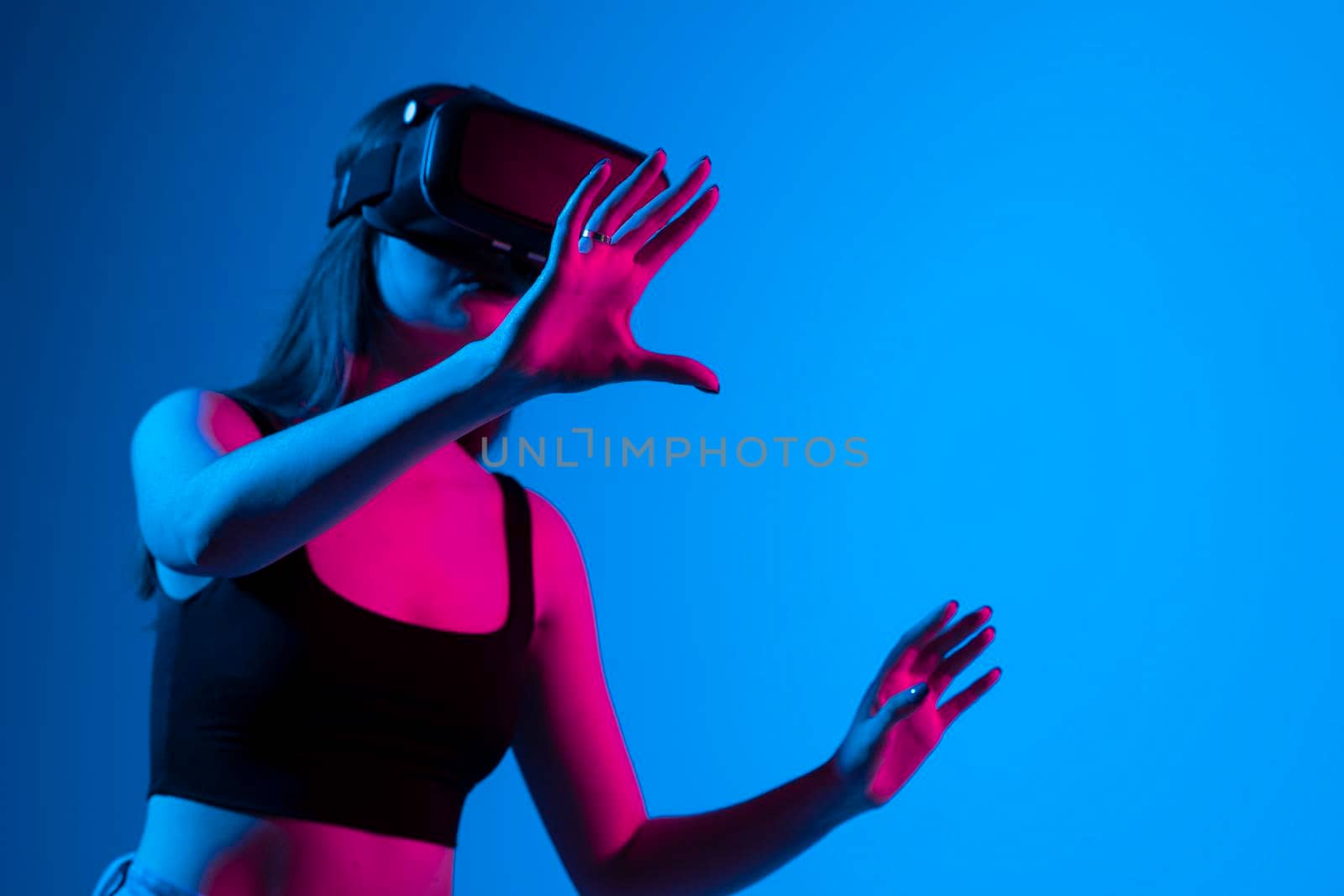 Young woman wearing virtual reality device in a neon light over a blue background. by vovsht