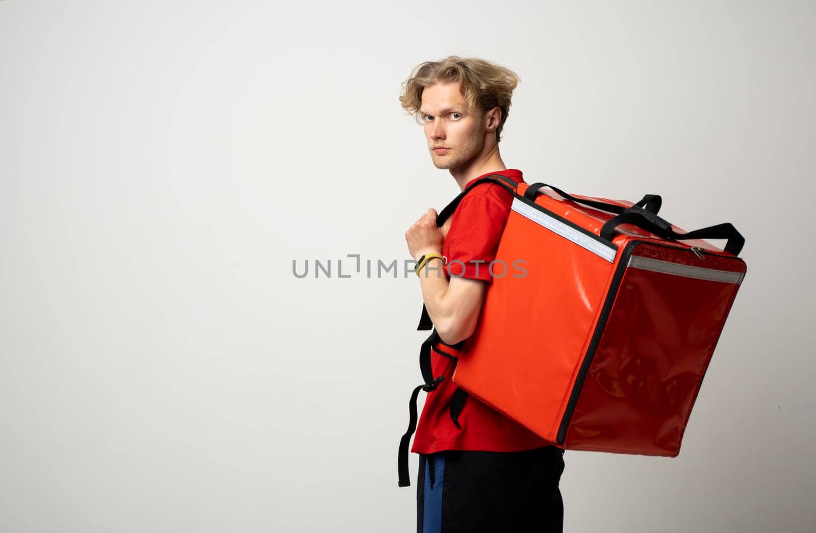 Delivery man employee man in a red tshirt uniform workwear work as a dealer courier and hold red thermal food bag backpack isolated on white background. Service concept. by vovsht