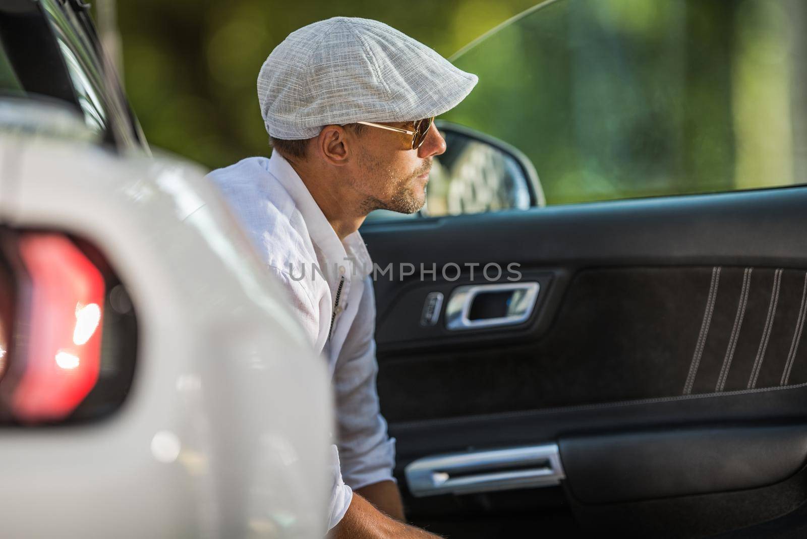 Young Caucasian Men Wearing Stylish Beret and Sunglasses Seating Inside His Modern Convertible Car and Enjoying the Moment. by welcomia