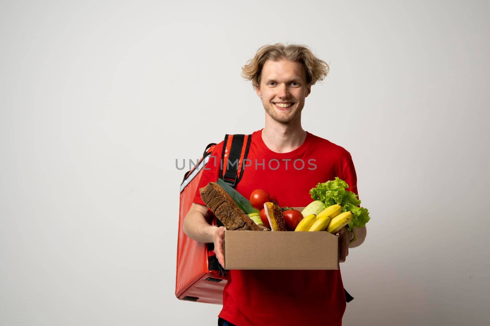 Handsome delivery man carrying package box of grocery food and drink from store. Isolated on white studio Background. Copy Space. Delivery Concept. by vovsht