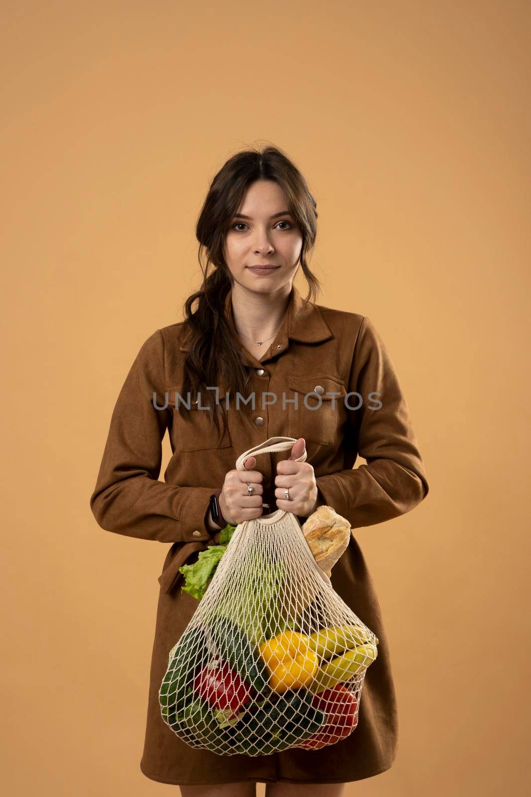 Zero waste concept. Young brunette woman holding mesh eco bag with organic fruits and vegetables. Using reusable crochet net bag for grocery shopping. by vovsht