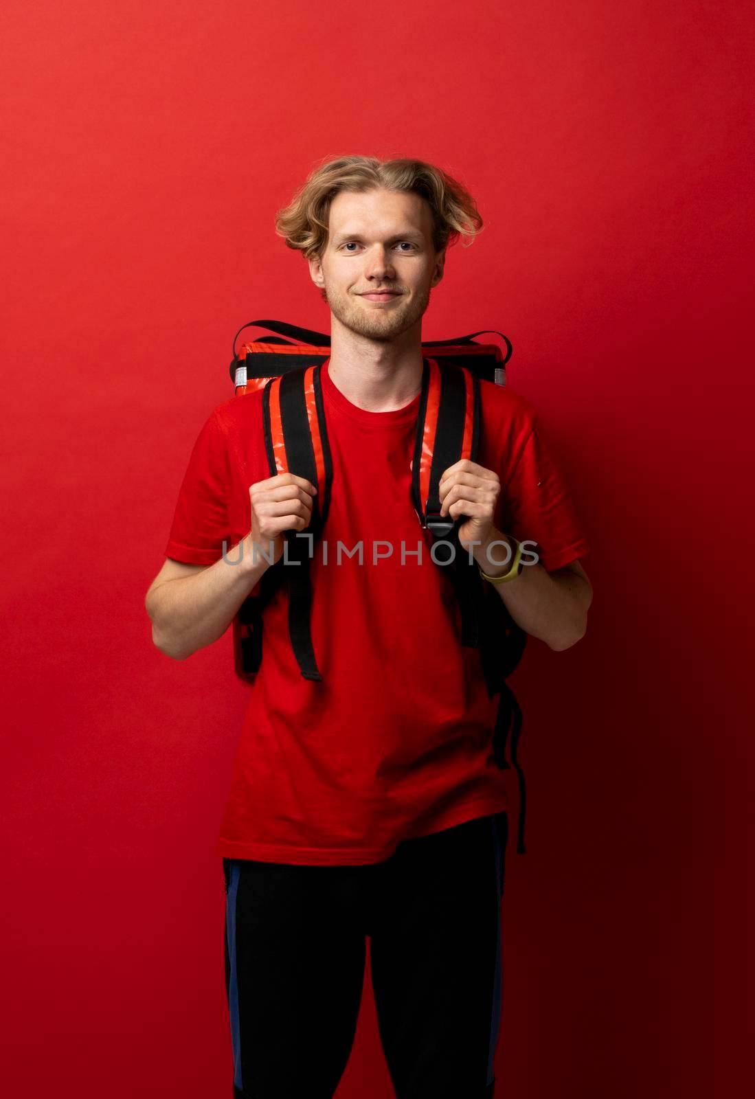 Delivery guy employee man in red uniform workwear work as dealer courier with a red thermal food bag backpack isolated on red color background studio. Service concept
