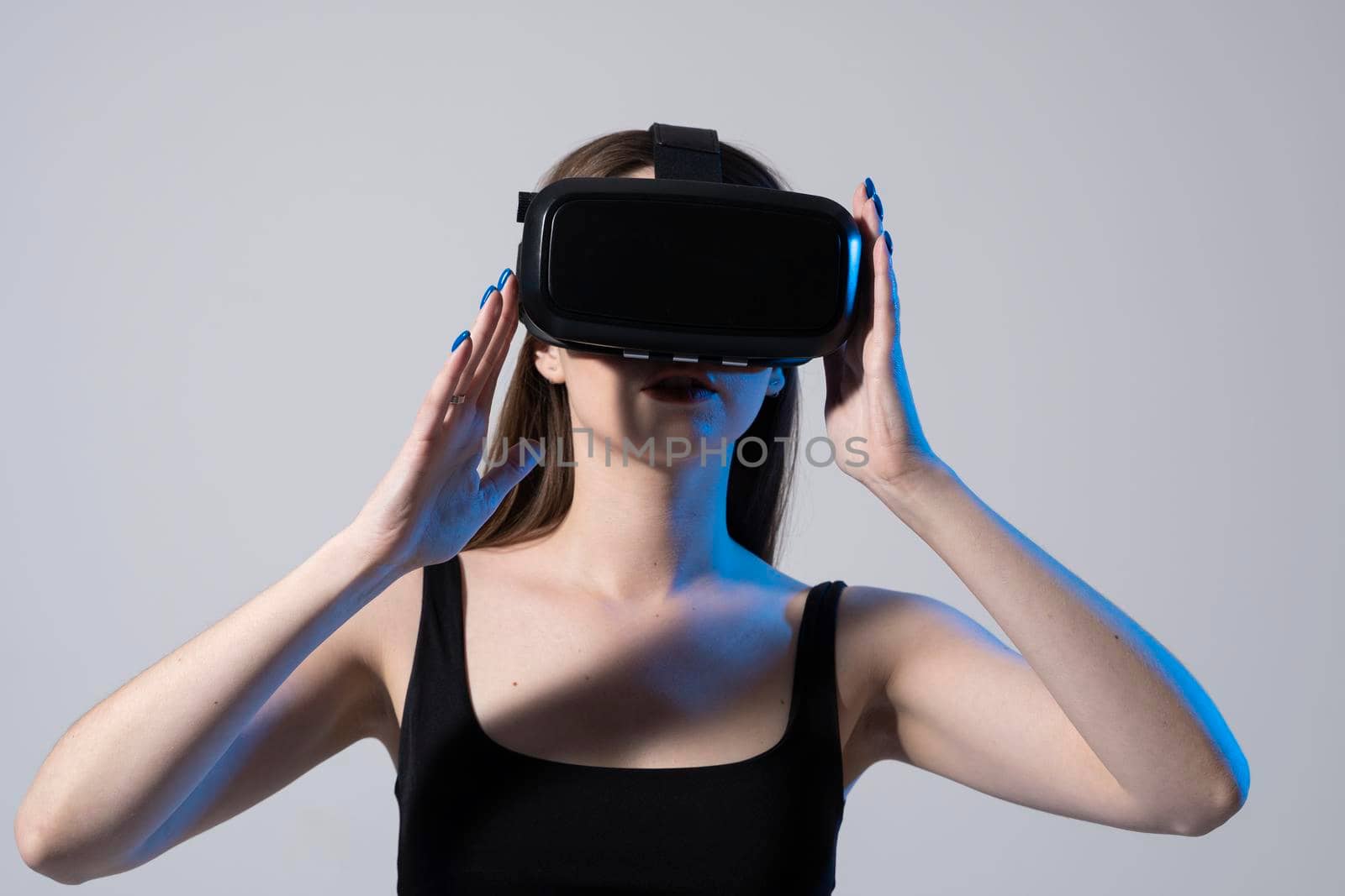 Business woman wearing VR goggles and interacts with metaverse using swipe and stretching gestures. Woman using virtual reality glasses in a studio. by vovsht