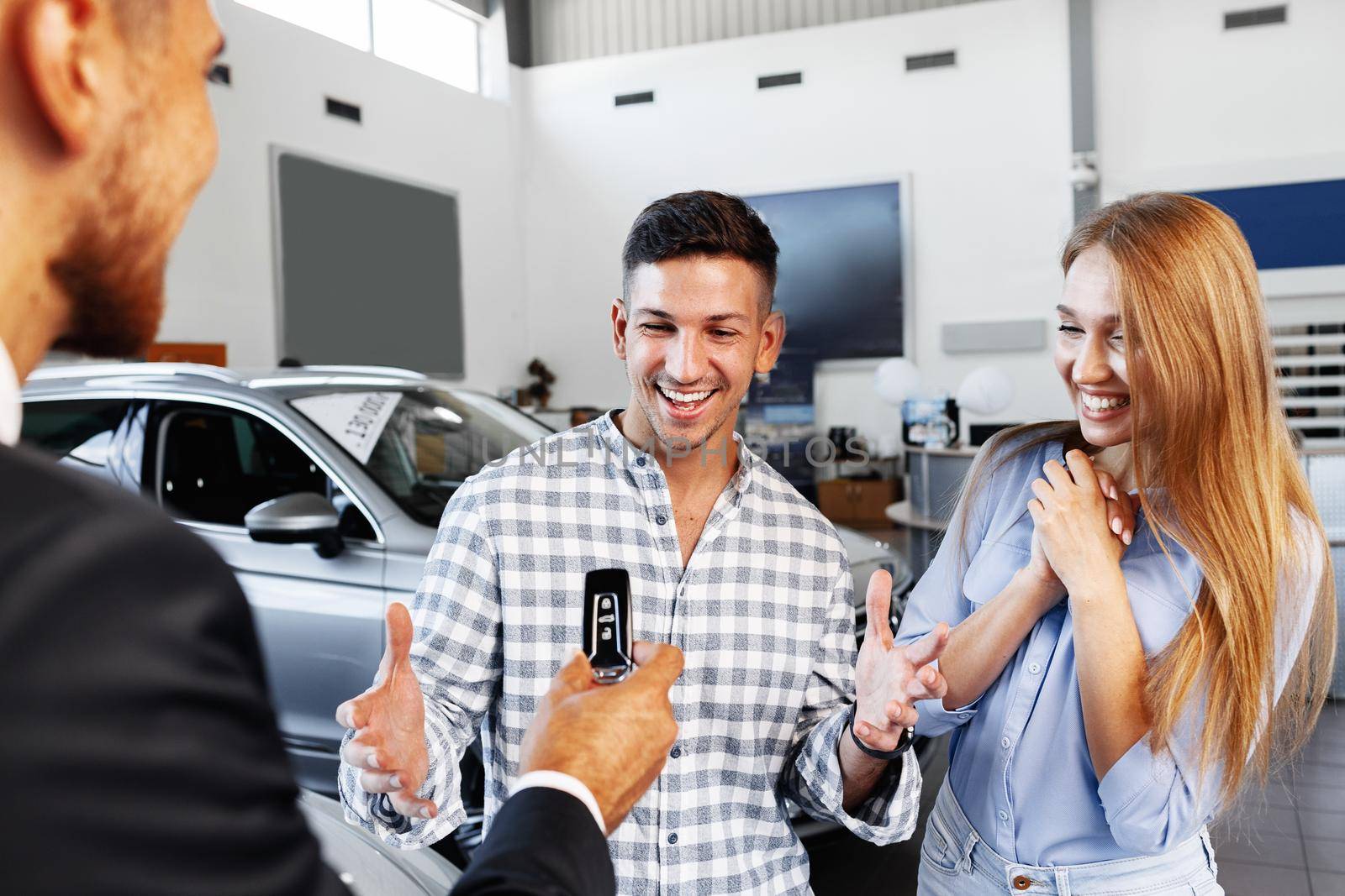 Cherrful young couple at the dealership buying a new car indoors