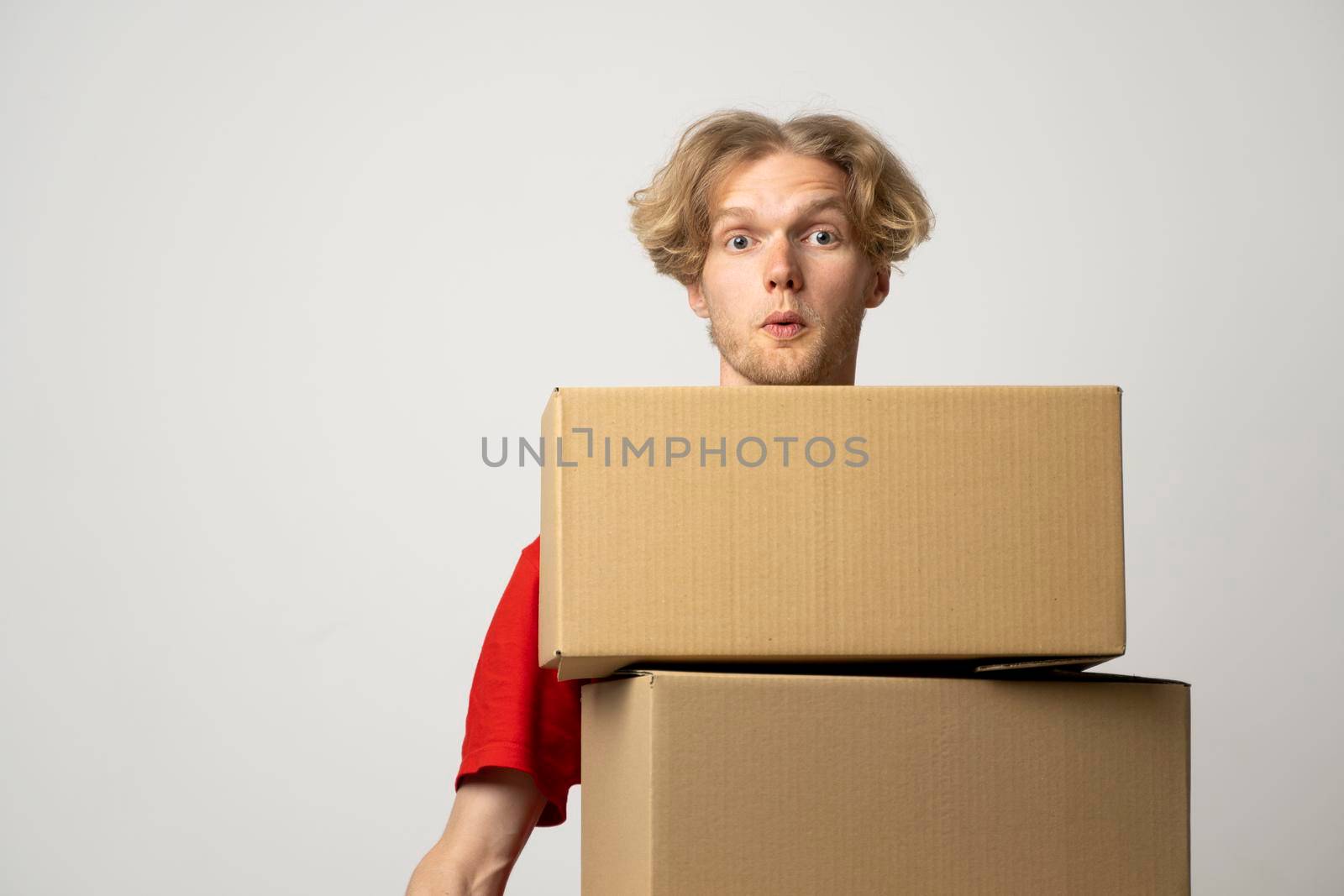 Cheerful delivery man. Happy young courier holding a cardboard boxes and smiling while standing against white background. Delivery man holding pile of cardboard boxes in front of himself