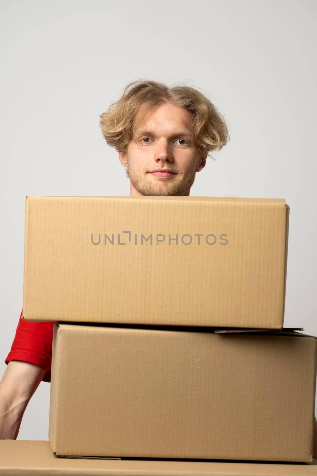 Cheerful delivery man. Happy young courier holding a cardboard boxes and smiling while standing against white background. Delivery man holding pile of cardboard boxes in front of himself. by vovsht