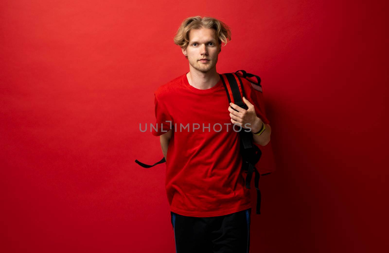 Portraite of delivery man in red uniform with thermo backpack bag isolated on red studio background. Shipment service