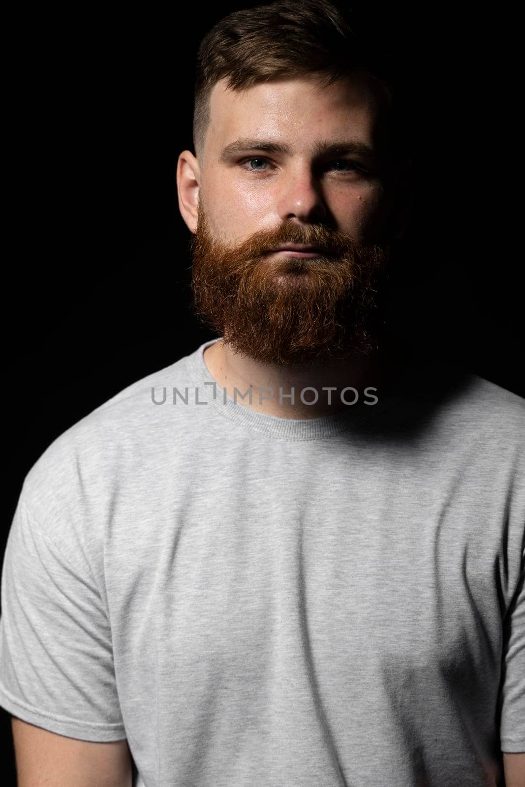 Portrait of handsome serious unshaven guy with long beard and handlebar moustache in grey t-shirt looking forward