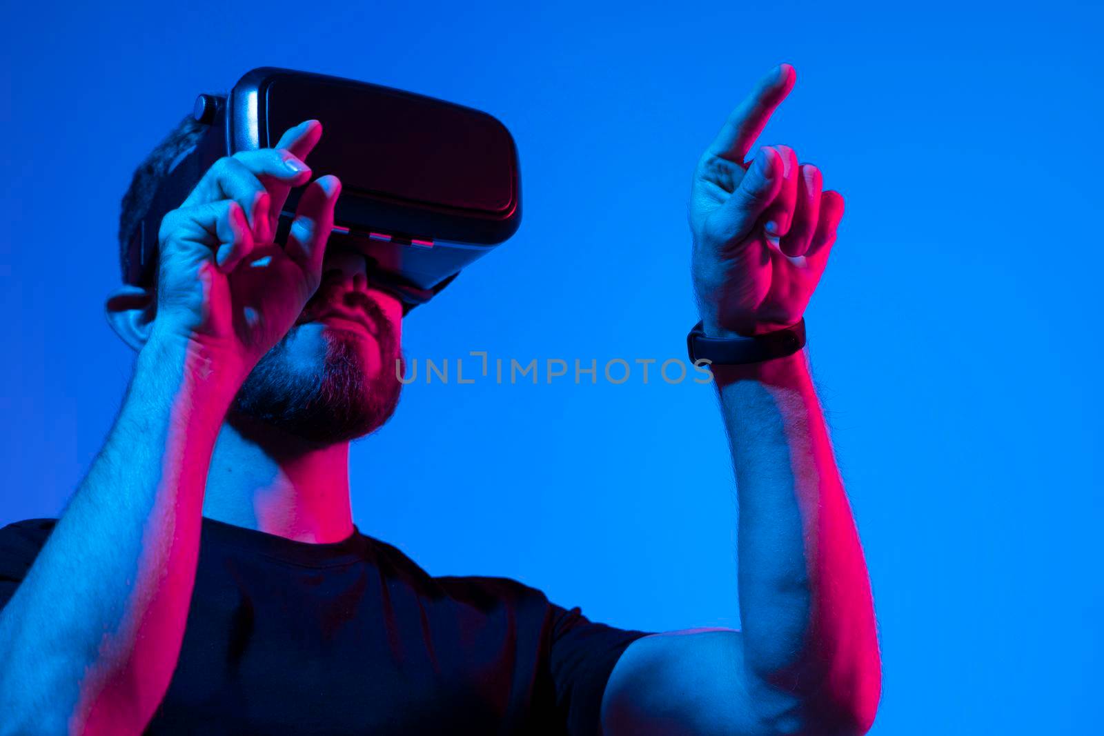 Young bearded man in virtual reality helmet plays online game in metaverse. Game simulates behavior in fictional world, gadgets and virtual reality addiction. Future technology concept. by vovsht