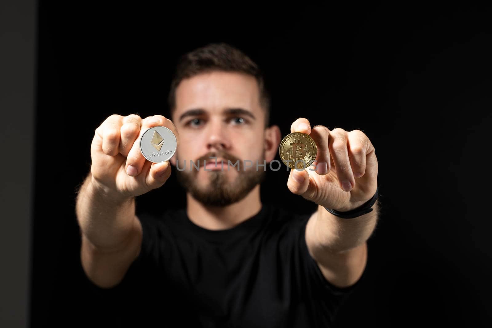 Young bearded man holding virtual currency ethereum coin and bitcoin. Cryptocurrency