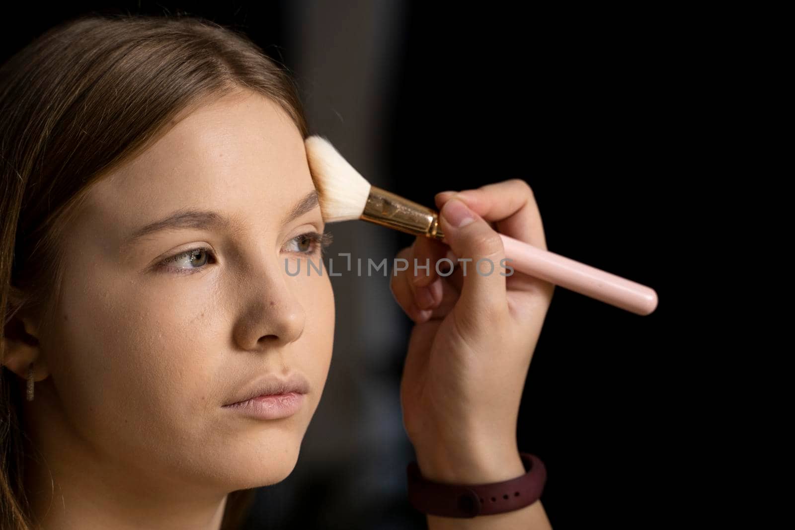 Close up face of beautiful young woman getting powder on her cheek with a brush. Professional makeup artist