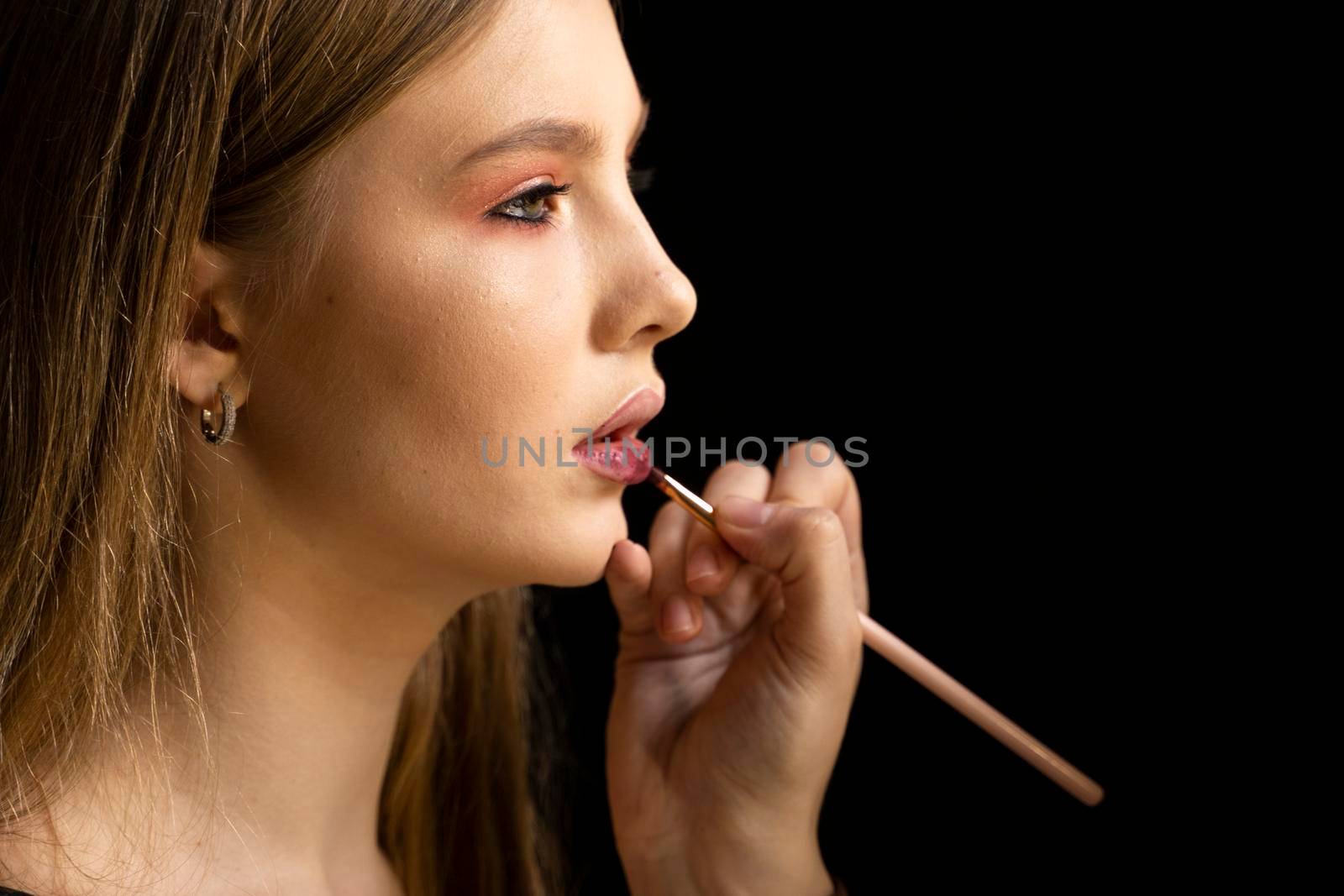 Makeup artist applies red lipstick on a beautiful woman face. Hand of make-up master, painting lips of young beauty model girl. Make up in process