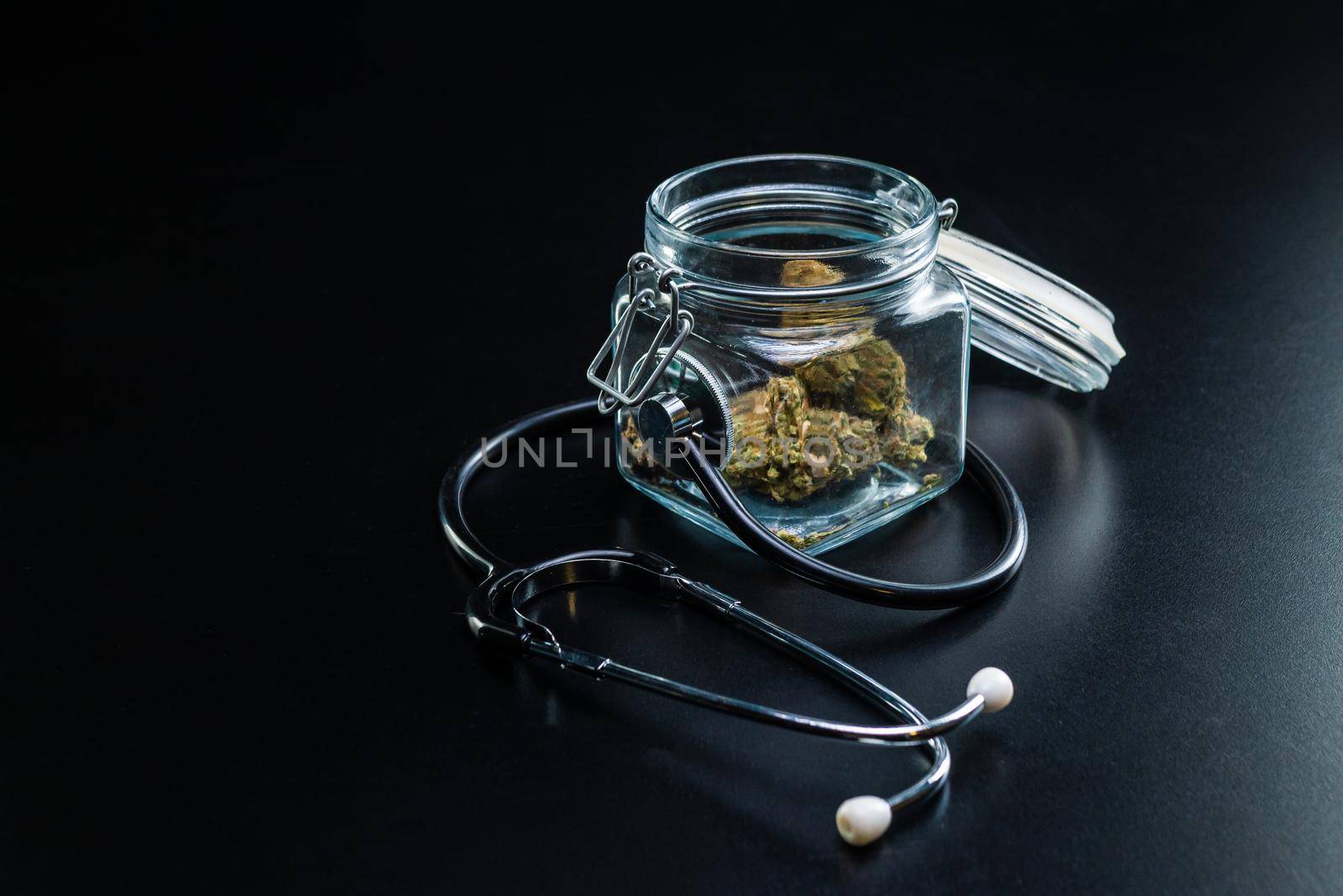 the Dry medical cannabis in a jar with a stethoscope on a black background