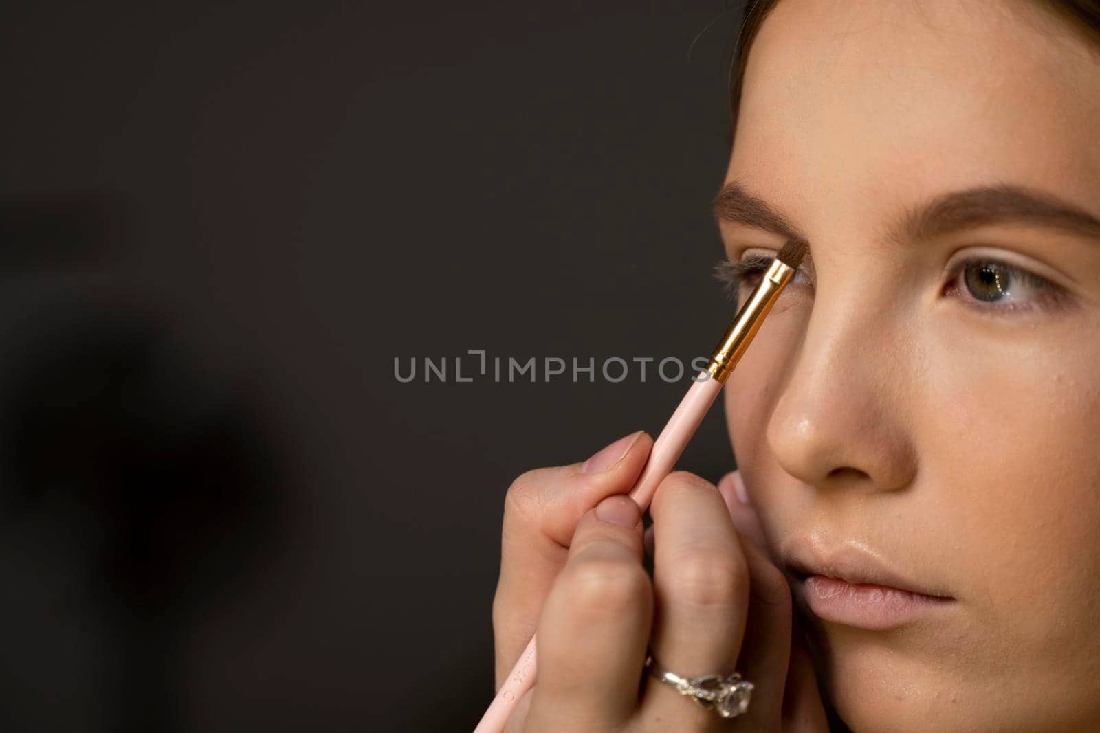 Makeup artist doing a eyebrows makeup on a beautiful woman face. Hand of make-up master is painting eyebrow of young beauty model girl. Make up in process. by vovsht