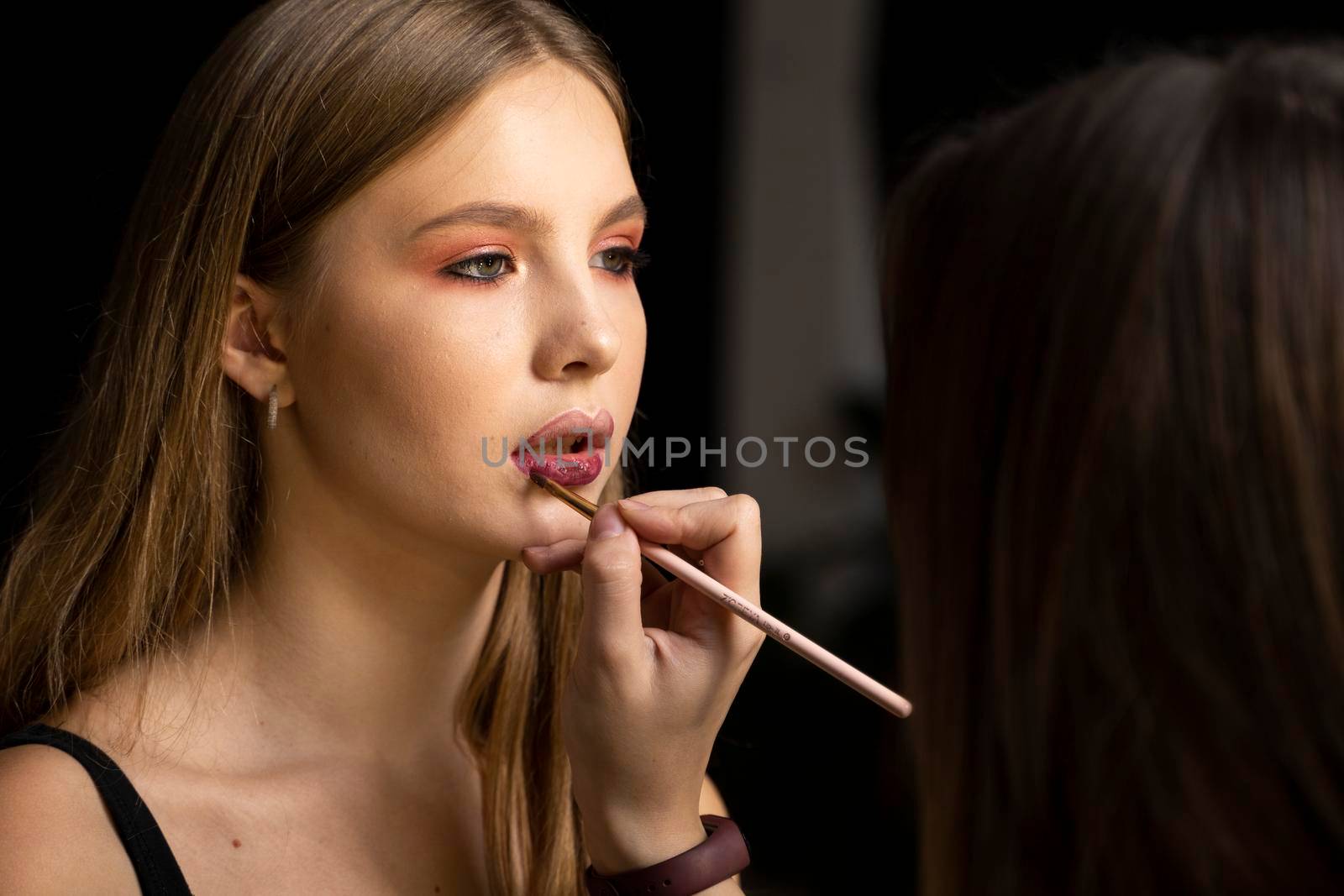 Makeup artist applies red lipstick on a beautiful woman face. Hand of make-up master, painting lips of young beauty model girl. Make up in process