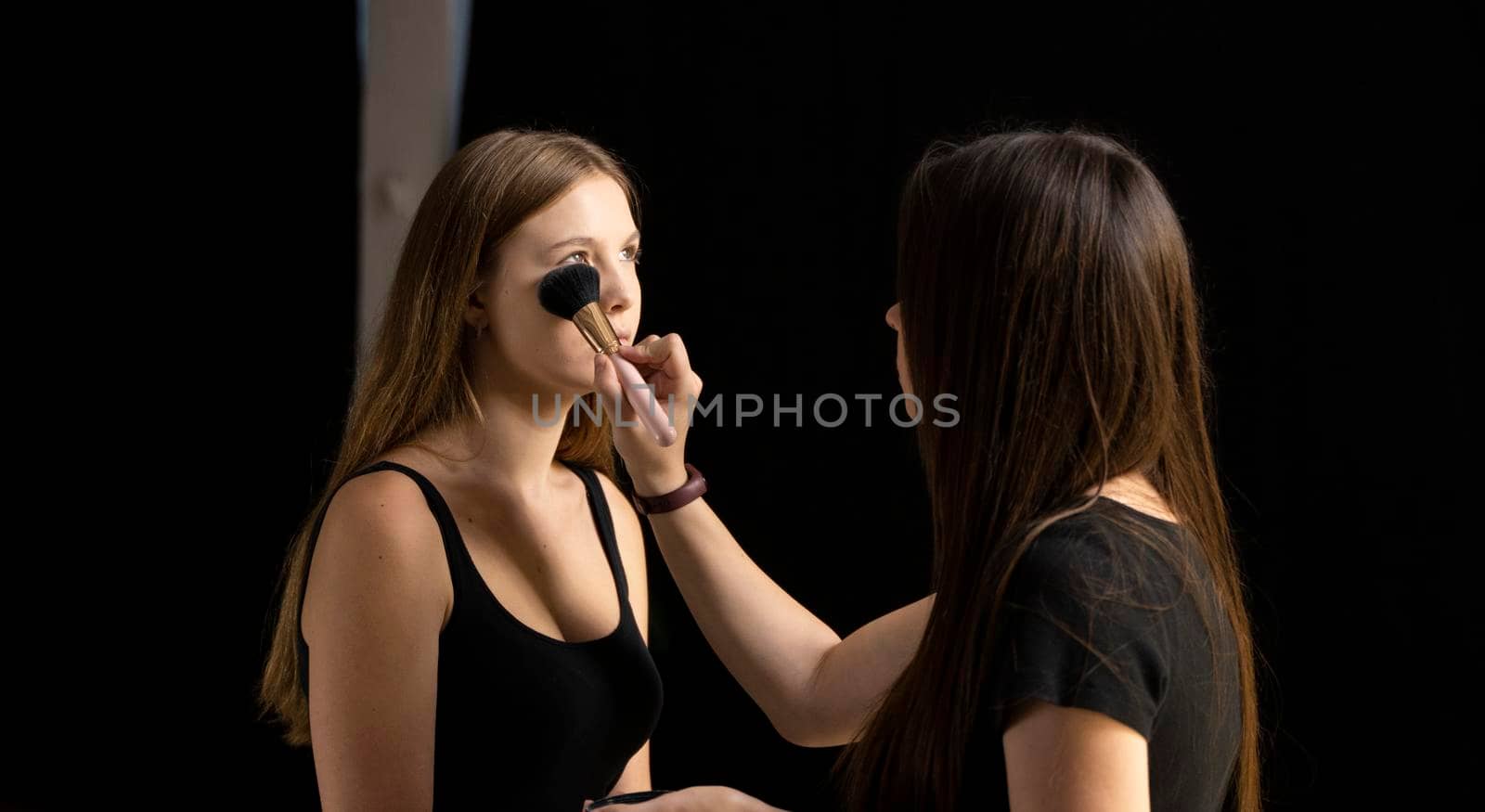 Close up face of beautiful young woman getting powder on her cheek with a brush. Professional makeup artist