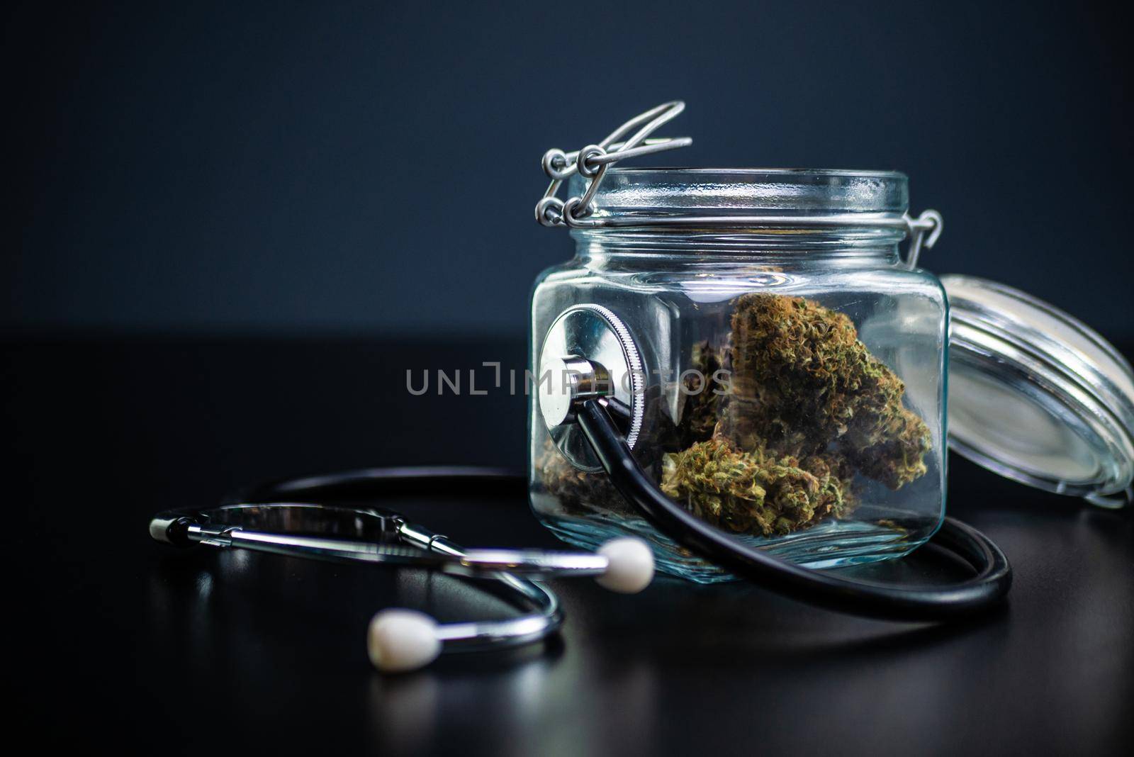 Dry medical cannabis in a jar with a stethoscope on a black background by Rotozey