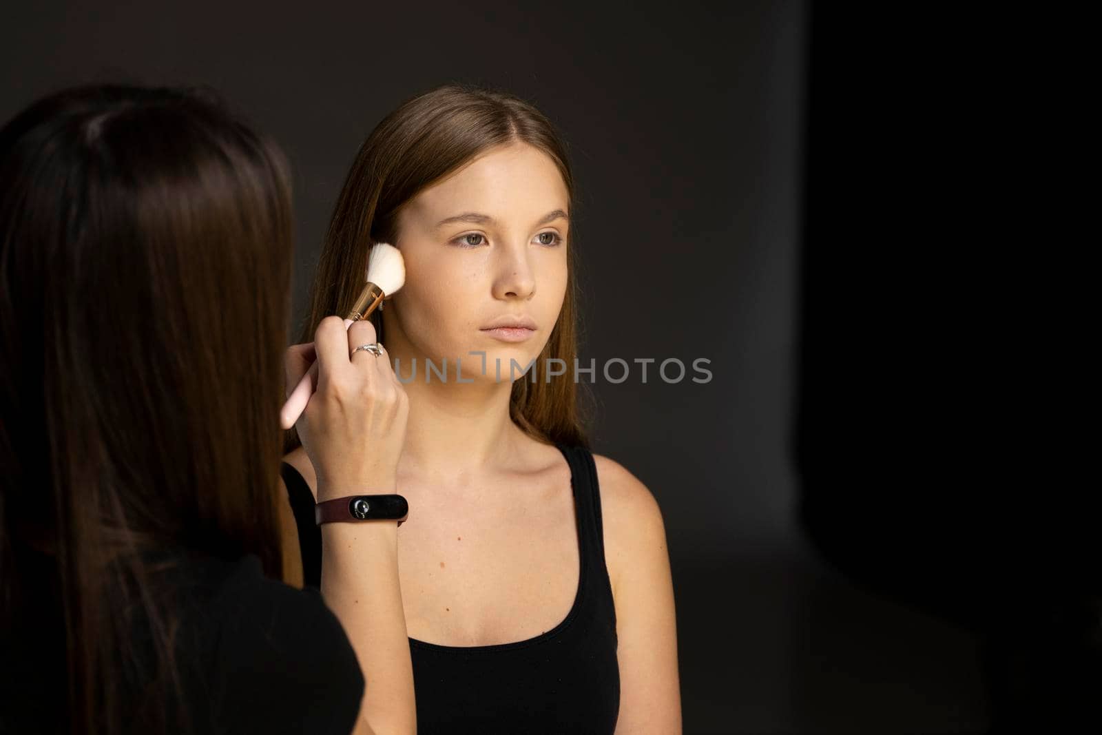 Make-up artist applying powder with a brush on model's cheeks. Professional make-up