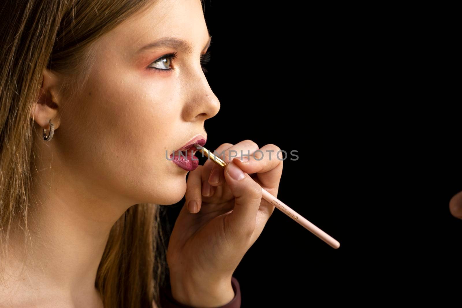 Makeup artist applies red lipstick on a beautiful woman face. Hand of make-up master, painting lips of young beauty model girl. Make up in process