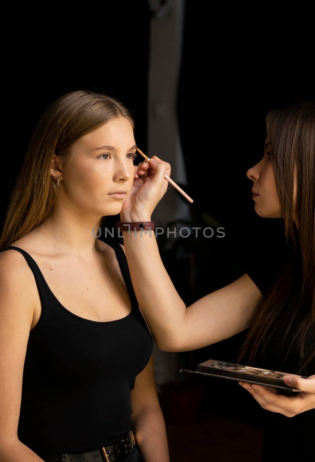 Makeup artist doing a eyebrows makeup on a beautiful woman face. Hand of make-up master is painting eyebrow of young beauty model girl. Make up in process