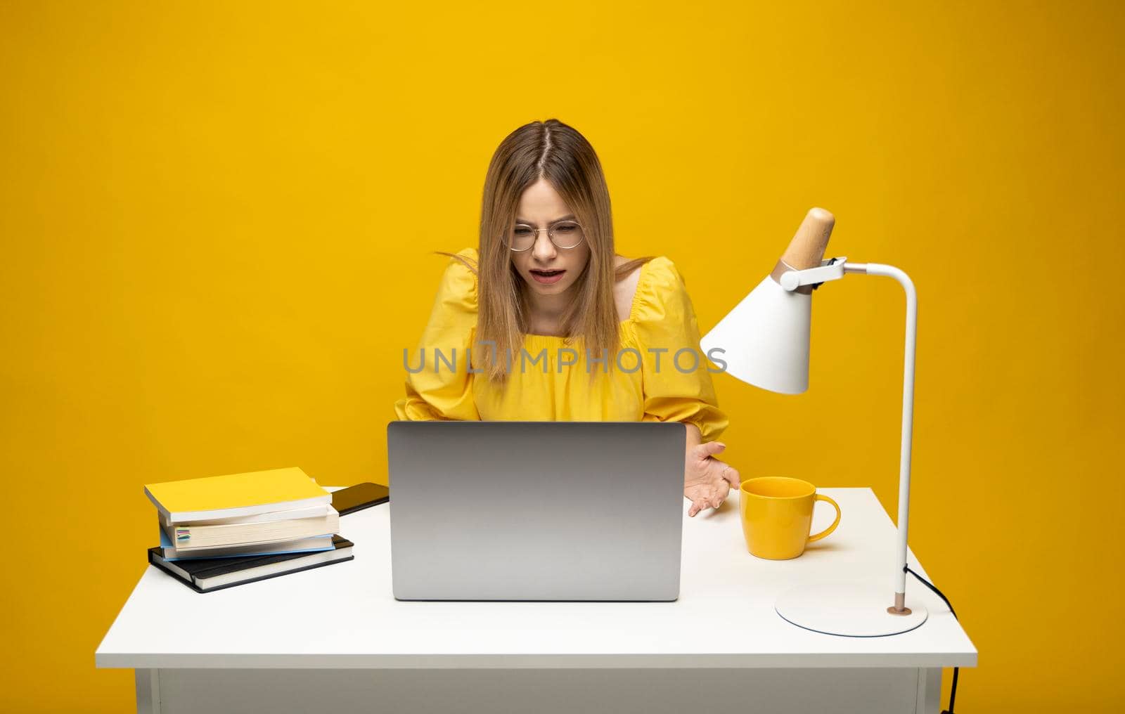 Young indignant confused secretary employee business woman with a spread hands in yellow shirt sit work at white office desk use pc laptop computer