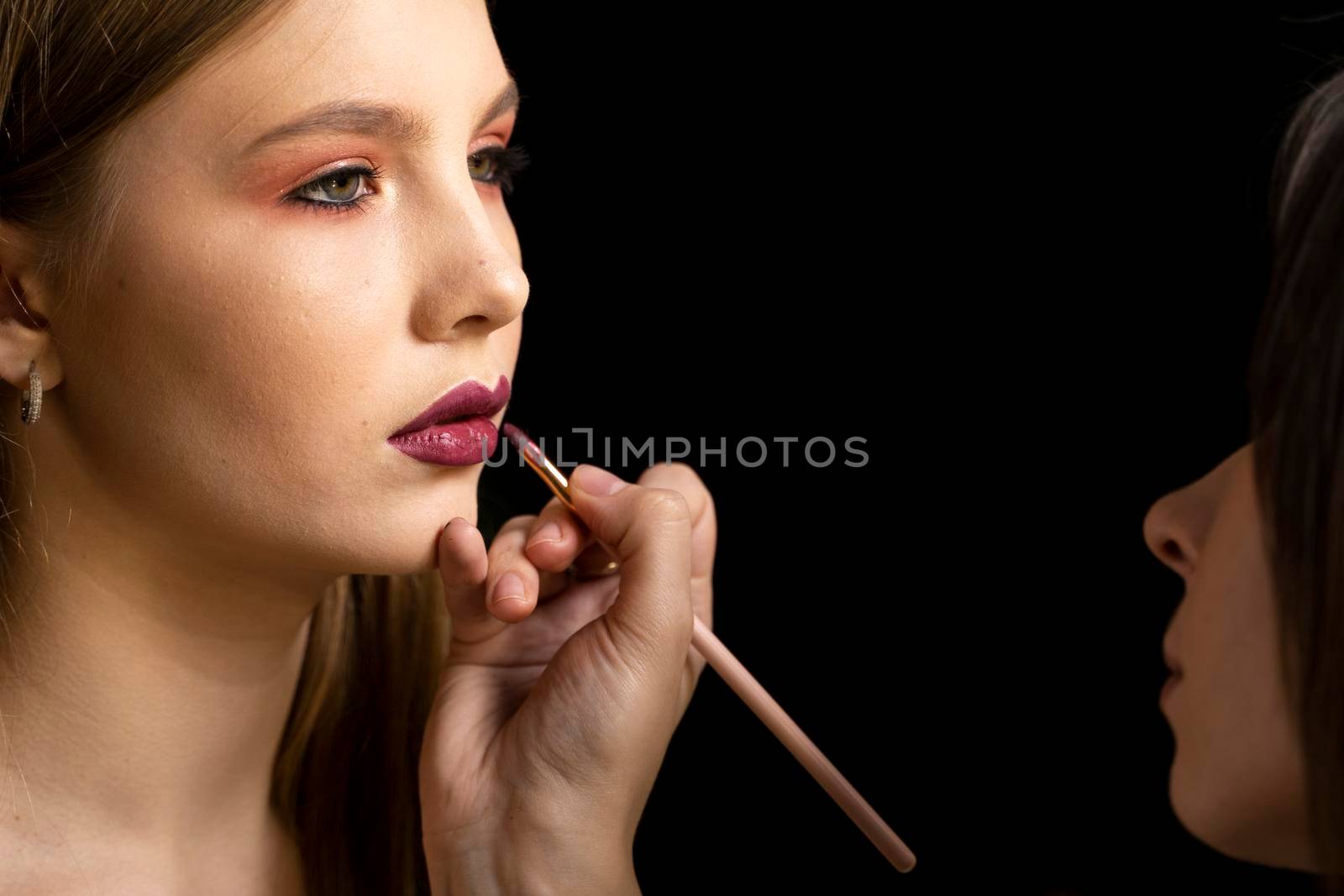 Makeup artist applies red lipstick on a beautiful woman face. Hand of make-up master, painting lips of young beauty model girl. Make up in process