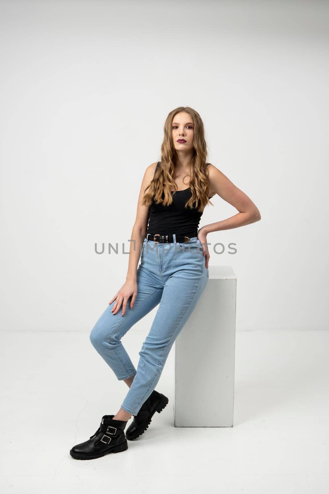 Beautiful young woman portrait in a black t-shirt and blue jeans. Studio shot, isolated on gray background. by vovsht