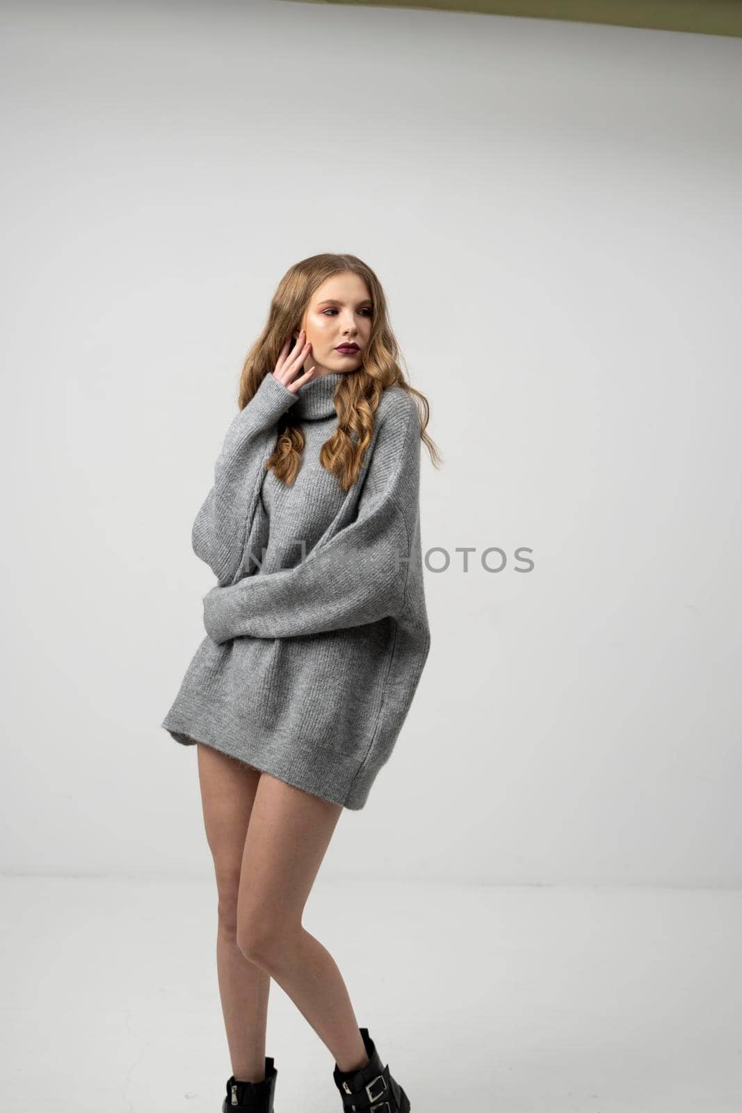 Beautiful young woman portrait in a long sweater. Studio shot, isolated on gray background. by vovsht