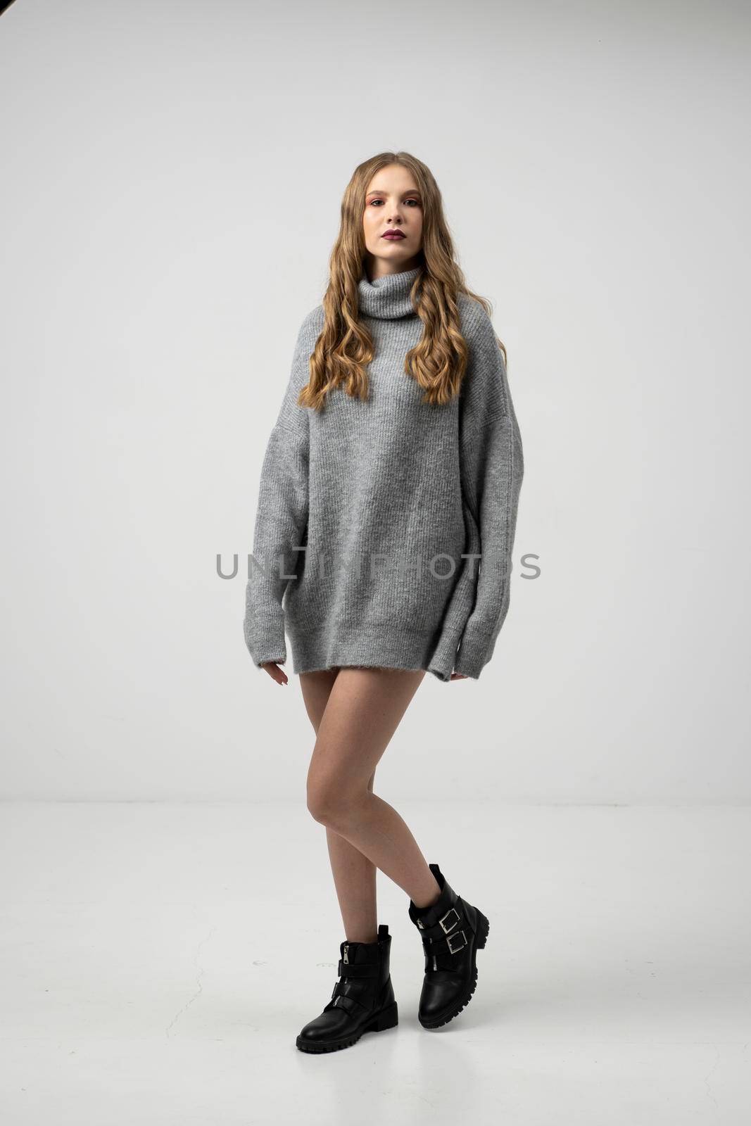 Beautiful young woman portrait in a long sweater. Studio shot, isolated on gray background. by vovsht