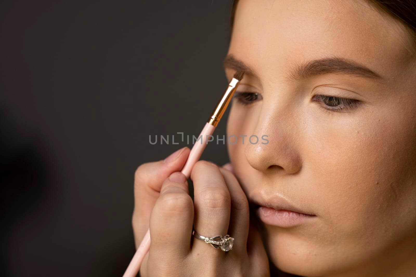 Makeup artist doing a eyebrows makeup on a beautiful woman face. Hand of make-up master is painting eyebrow of young beauty model girl. Make up in process